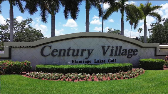 Sign for Century Village with Flamingo Lakes Golf, surrounded by palm trees and landscaped area.