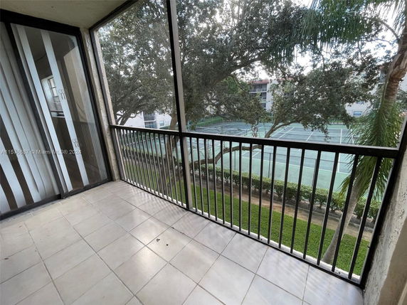 View of tennis courts from a balcony with tile flooring and metal railing.
