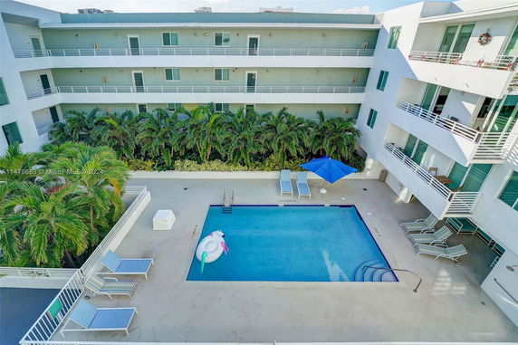 Outdoor swimming pool in the courtyard of an apartment complex with lounge chairs and palm trees.
