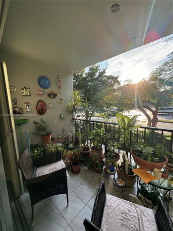Balcony with chairs and plants offering a view of trees and street.