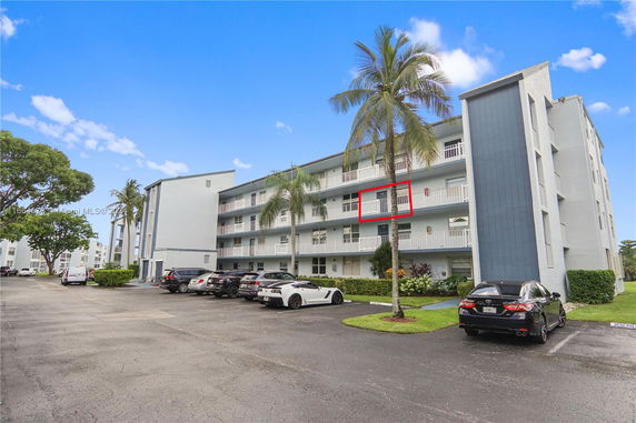 Front view of a multi-story building with balconies and a parking area.