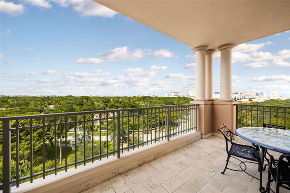 Panoramic view from a balcony with decorative railing overlooking a green landscape and city skyline.