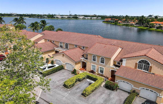 Aerial view of townhouses with red-tiled roofs by a lakeside.