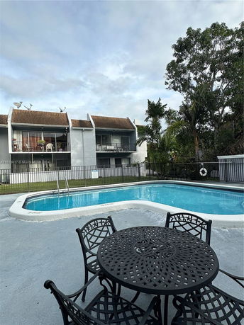Outdoor swimming pool with a metal table and chairs in the foreground, and a residential building in the background.