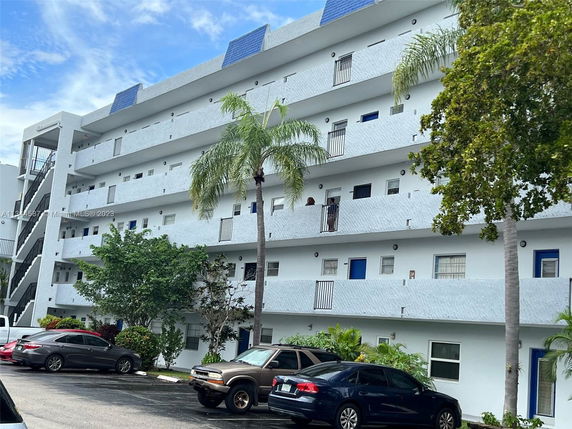 Front view of a multi-story residential building with balconies and a parking area in front.