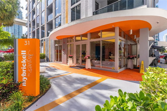 Front view of a modern building entrance with large glass doors and orange accents.