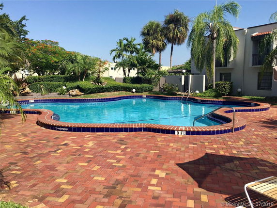 Outdoor swimming pool with surrounding brick patio and lush greenery.