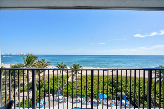 View of the ocean from a balcony with beach and palm trees below.