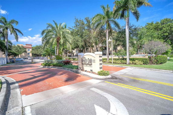 Front view of a condominium complex entrance with a sign and driveway.