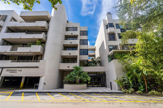 Front view of a multi-story building with balconies and a parking area.