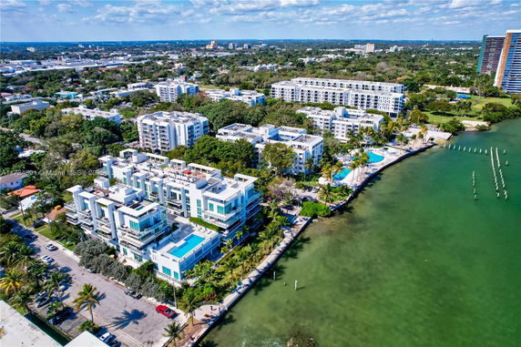 Aerial view of a residential area by the water with modern multi-story buildings and greenery.