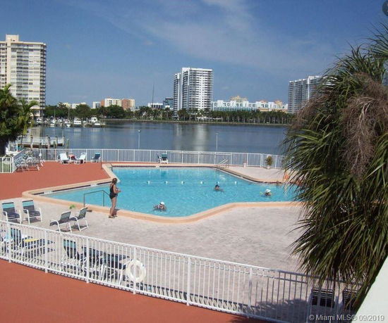 View of a swimming pool area with high-rise buildings in the background near a waterfront.
