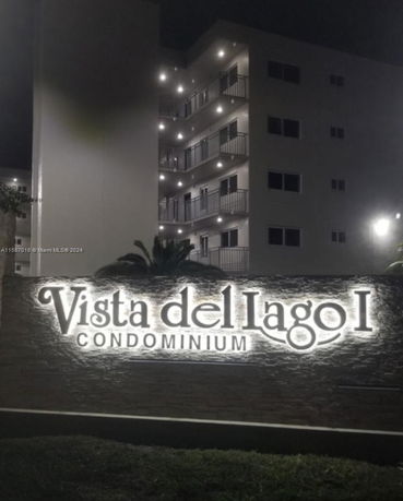 Front view of a multi-story condominium building at night with illuminated balconies.