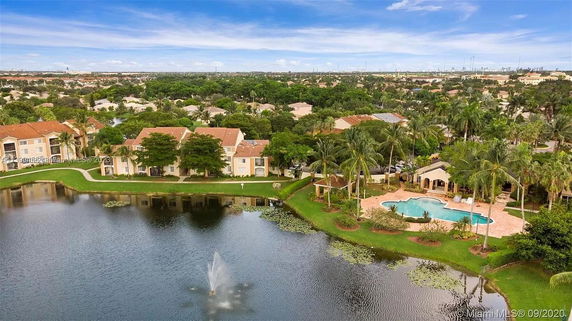A scenic aerial view of a residential area with a lake and swimming pool surrounded by trees and buildings.