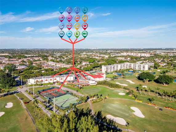 Panoramic view of a tennis court, golf course, and residential buildings in a suburban area.