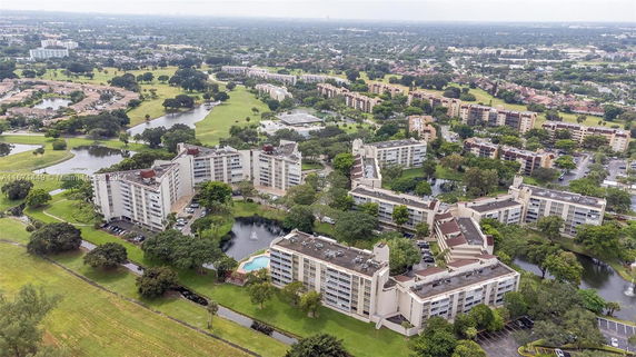 Aerial view of multiple residential buildings surrounded by greenery and water features in a suburban area.