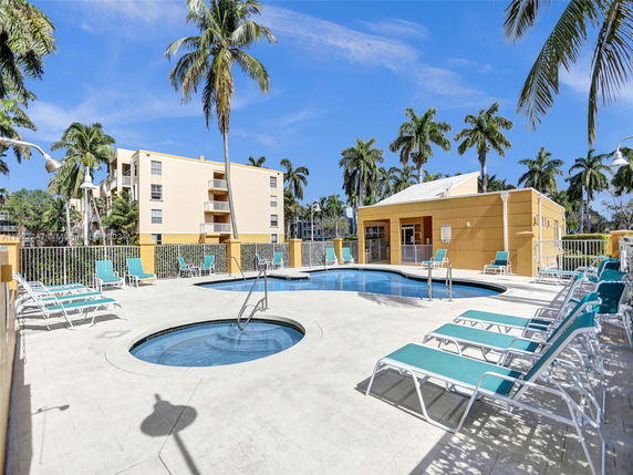 Outdoor swimming pool area with lounge chairs and surrounding palm trees.