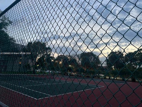 Tennis court with a chain-link fence surrounding it, trees in the background.