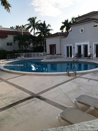 Outdoor swimming pool area adjacent to a building with palm trees in the background.
