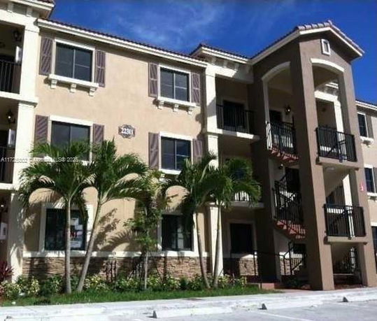 Front view of a multi-story building with balconies and palm trees.