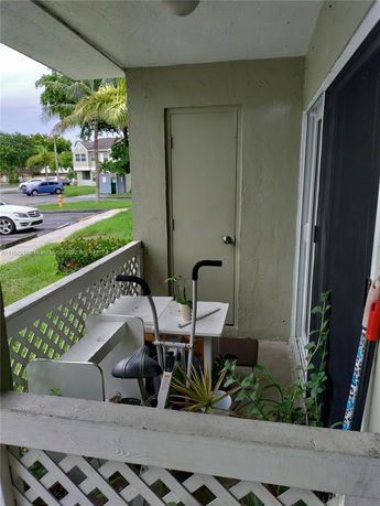 Outdoor area with a small covered patio and a door, containing various items and plants.