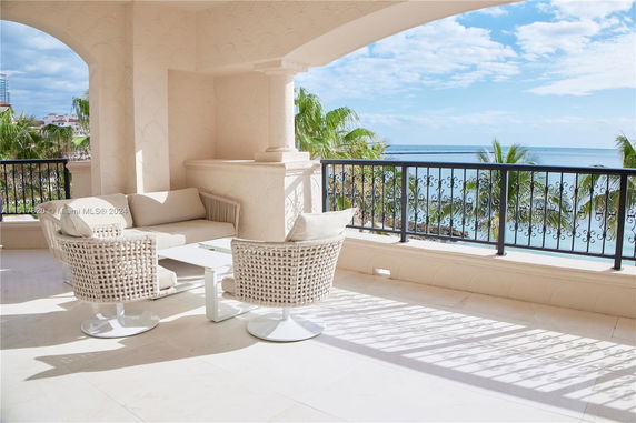 Outdoor seating area on a balcony with a view of the ocean and palm trees.