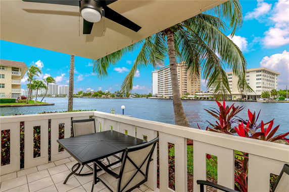 View from a patio overlooking water with buildings and palm trees in the background.