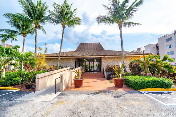 Front view of a building with a stone facade and tiled roof, surrounded by palm trees.