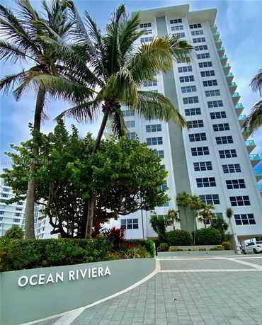 Front view of a tall residential building with palm trees at the entrance.