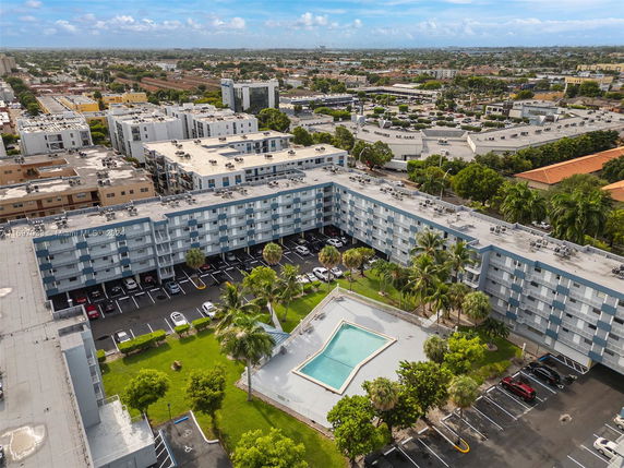 Aerial view of a large residential complex with swimming pool and surrounding cityscape.
