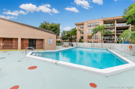 Outdoor swimming pool area with adjacent building and fenced surroundings.