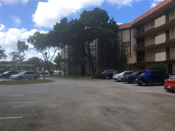 Outdoor parking lot with several cars parked around a multi-story building.