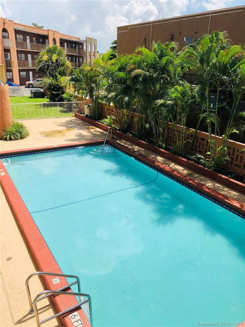 Outdoor swimming pool surrounded by plants and apartment buildings.