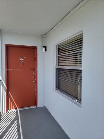 Entryway of a building with an orange door and a window with blinds.