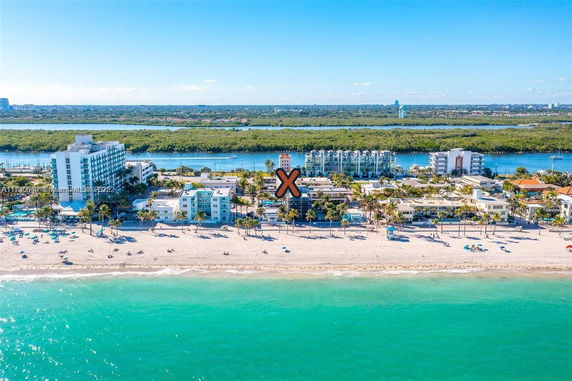 Aerial view of beachfront buildings with ocean and greenery in the background.