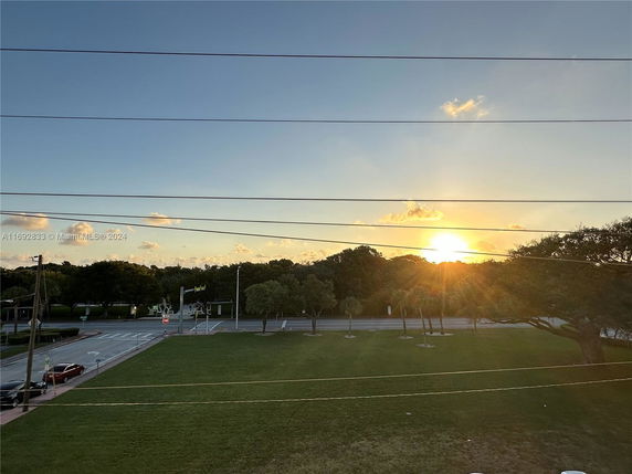 Panoramic view of a sunset over a tree-lined street with open grassy area.