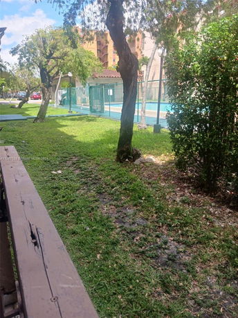 View of a fenced swimming pool area in an outdoor setting with trees and grass.