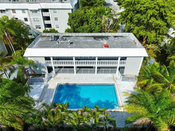 Aerial view of a building with a rectangular swimming pool in front.