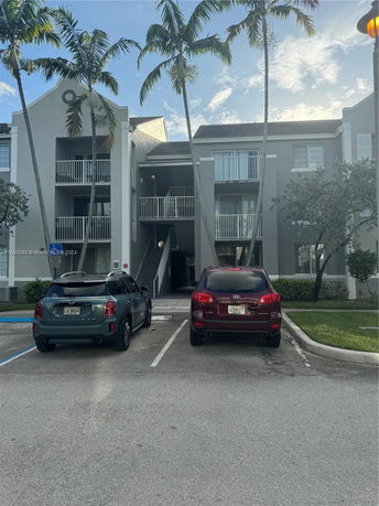 Front view of a multi-story residential building with balconies and two parked cars.