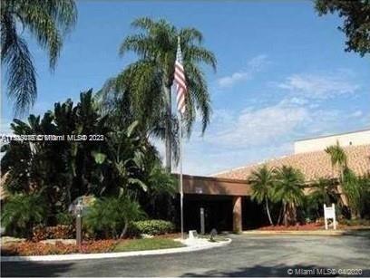 Front view of a building with a flat roof, an entrance canopy, and palm trees around it.