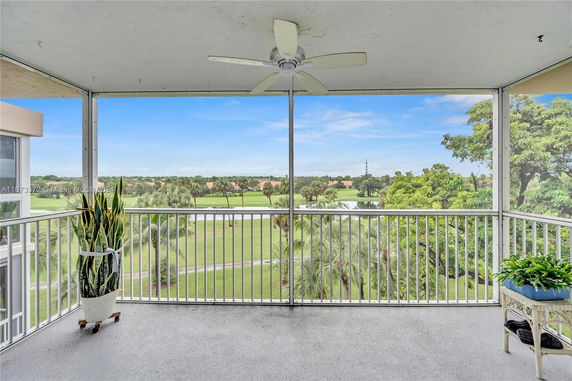 Outdoor balcony with a ceiling fan overlooking a scenic landscape with greenery and distant houses.