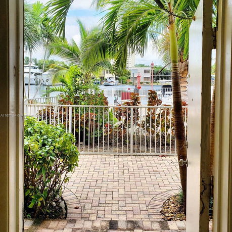 View through a doorway showing a patio with brick flooring, palm trees, and a railing overlooking a marina.