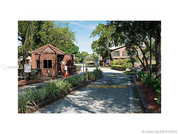 Gated entrance with a guardhouse and trees along the road.