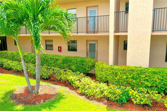 View of a two-story building with balconies and a green hedge.