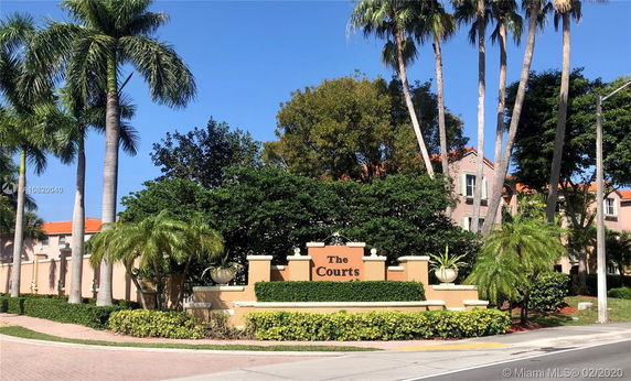 Front entrance view of a residential complex with a sign reading 'The Courts' surrounded by palm trees.
