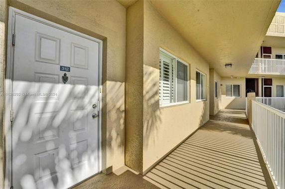 Exterior corridor of a residential building with a white door and beige walls.