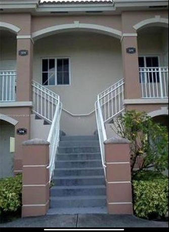 Front view of a house with arched entry and staircase leading up.