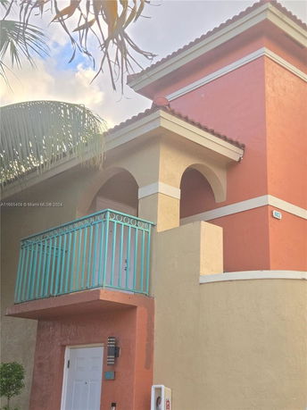 Front view of a building with an orange and beige facade and a balcony with teal railing.