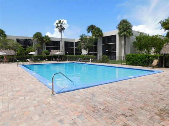 Swimming pool area with adjacent building and palm trees.
