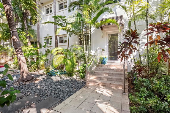 Front view of a building with steps leading to an entrance, surrounded by tropical plants.